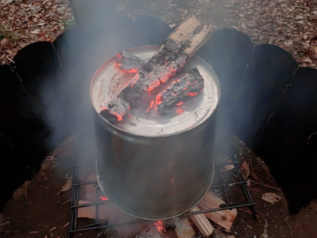 ビア缶チキンの作り方はキャンプ当日、火が安定したらチキンをビールを半分くらい残した缶をセットしたビア缶チキンスタンドに刺して、火の上に置いて、バケツを被せて40分から1時間程度焼き、バケツの上には炭を置く。